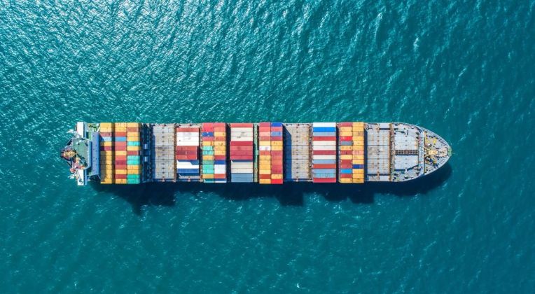 Aerial view of a container ship with colorful containers sailing through deep blue water.