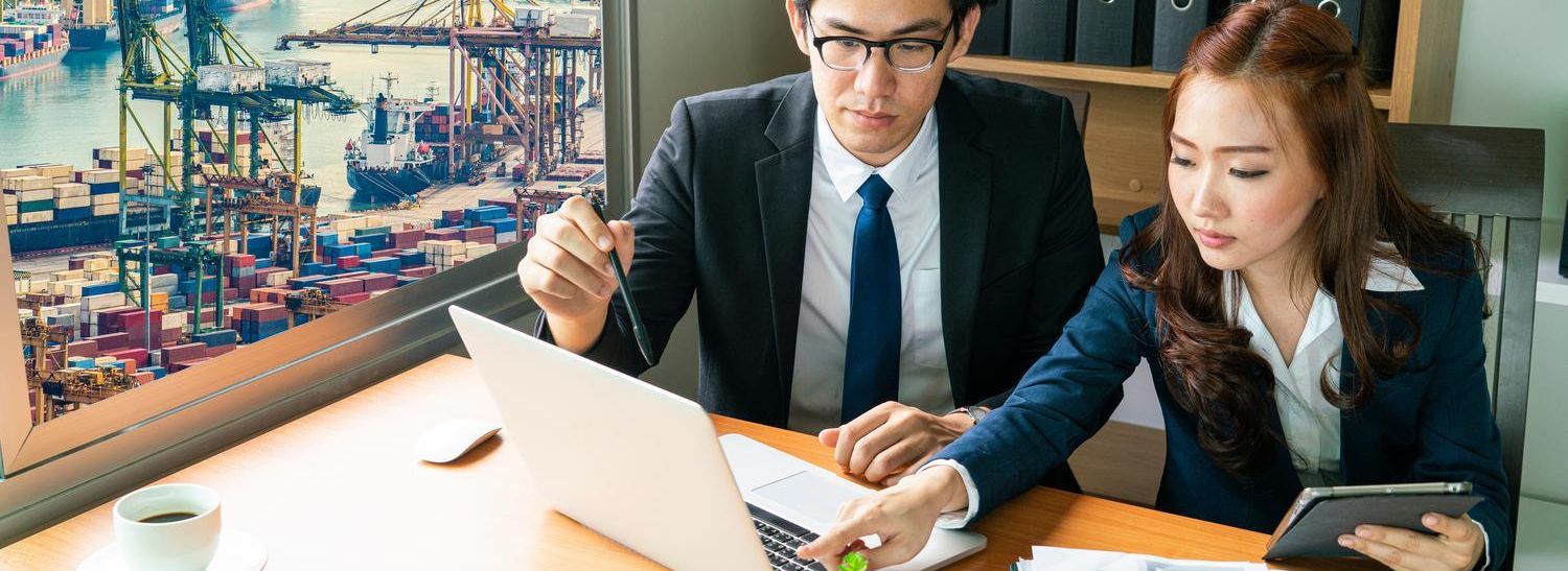 wo business professionals in an office with a laptop, a checklist, and a tablet, with a port featuring cranes and containers in the background.