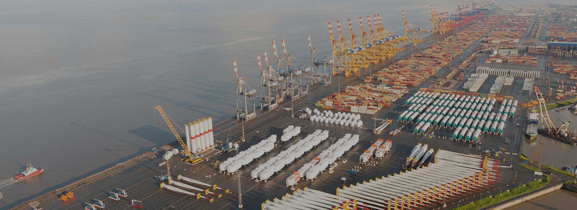 Aerial view of Bremerhaven container port with cranes, containers, and large-scale stored goods such as wind turbine blades.