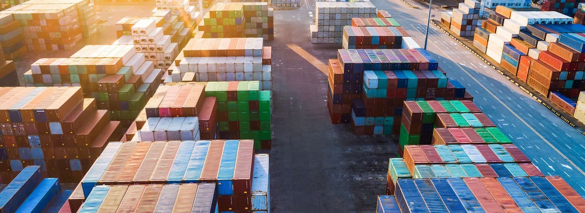 Aerial view of a container terminal at sunset with stacked containers and open driving lanes.