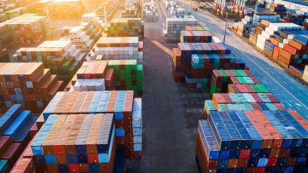 Aerial view of a container terminal at sunset with stacked containers and open driving lanes.