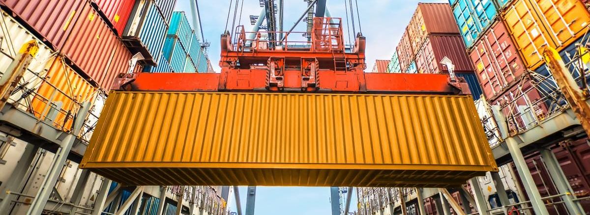 Close-up of a yellow container being moved by a crane in a container terminal, surrounded by stacked containers.