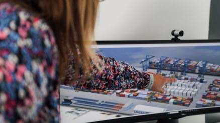 A woman pointing at a screen displaying a 3D visualization of a container terminal represented as a digital twin.