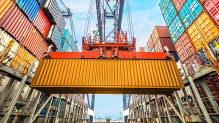 Close-up of a yellow container being moved by a crane in a container terminal, surrounded by stacked containers.