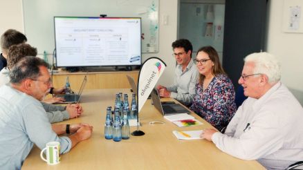 A team of professionals sitting in a conference room, discussing port logistics and viewing a presentation on a screen.