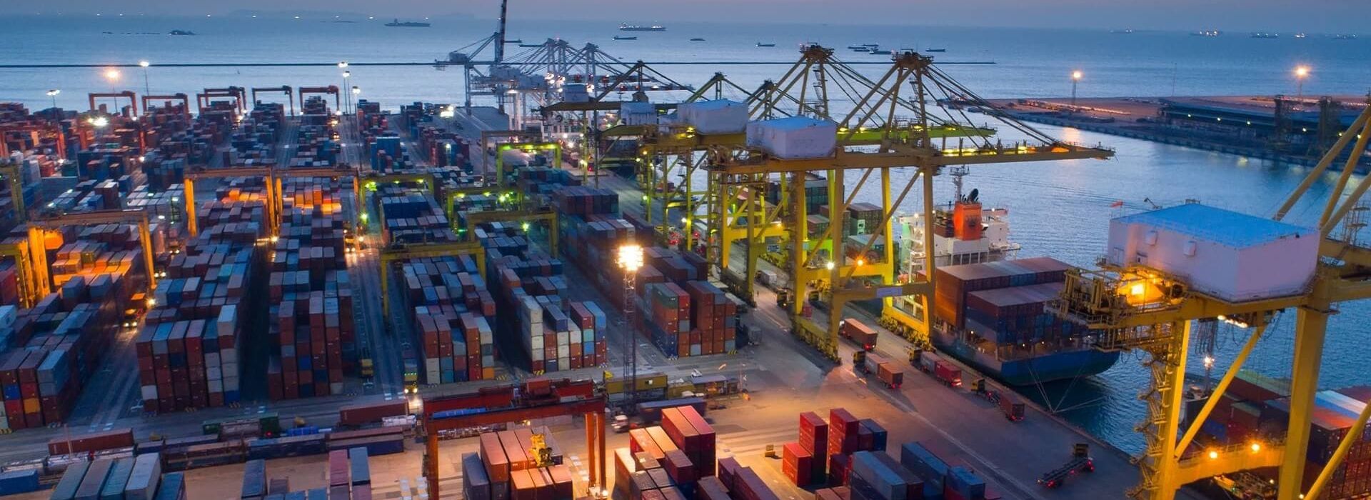 Container terminal at sunset with illuminated cranes and stacked containers, showcasing the efficiency of CHESSCON Yard View.