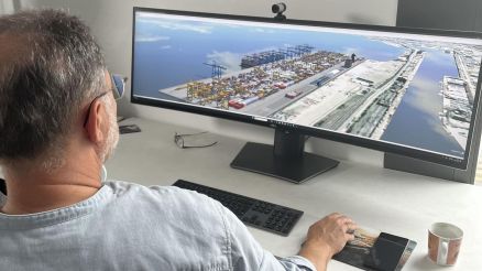 A man sitting at a desk working with a 3D visualization of a container terminal on a wide monitor.